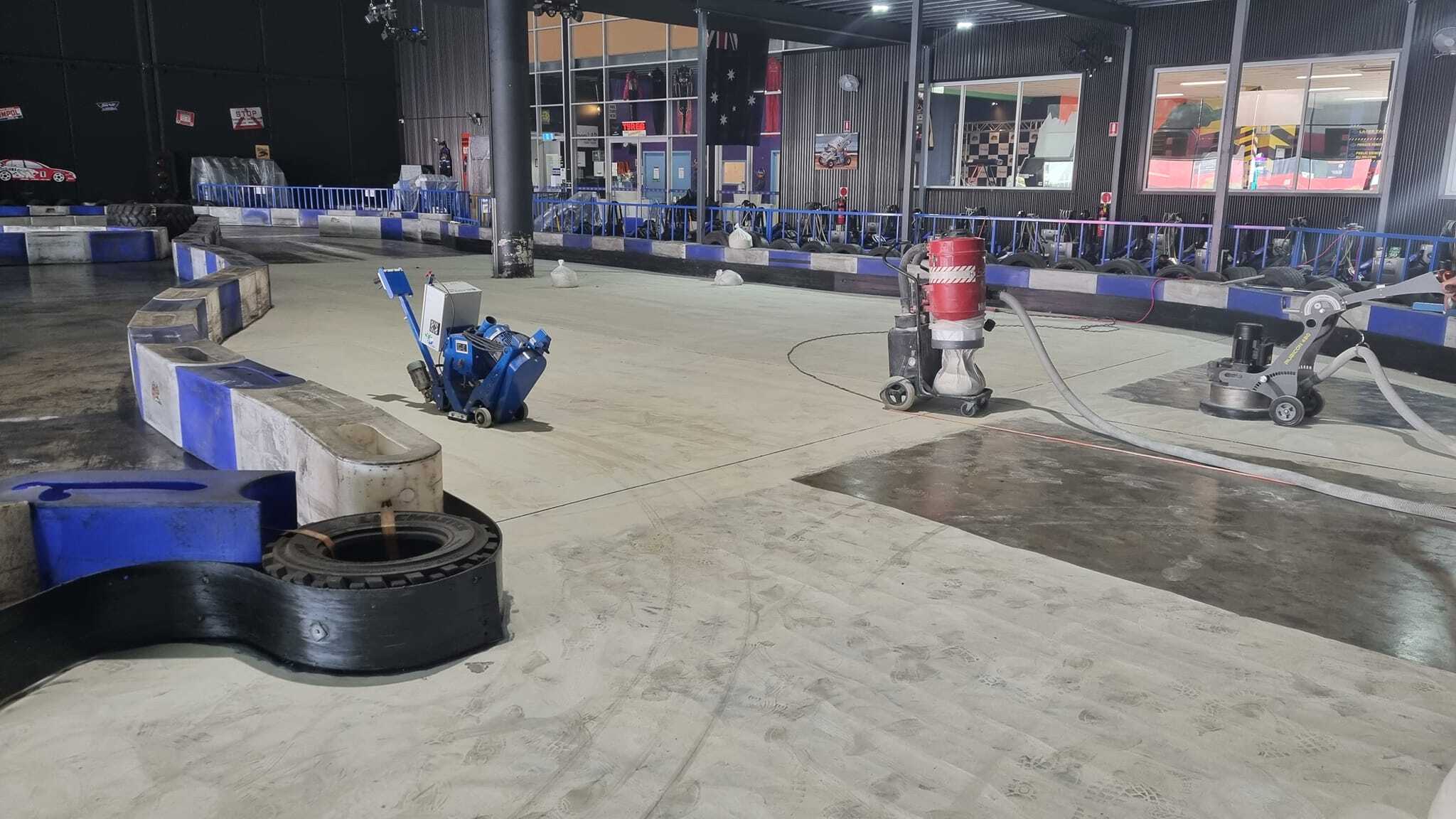 Floor grinders and a vacuum unit beside the barriers of an indoor kart track