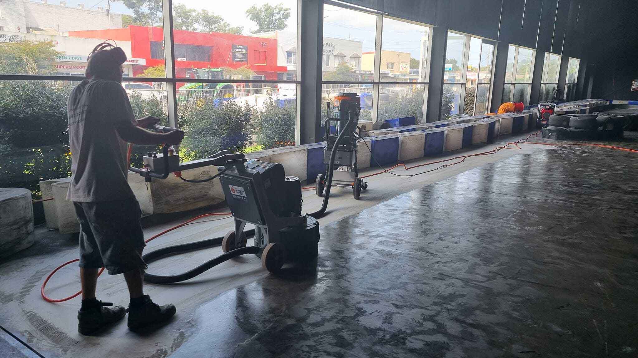 Worker grinding a concrete floor beside large shopfront windows