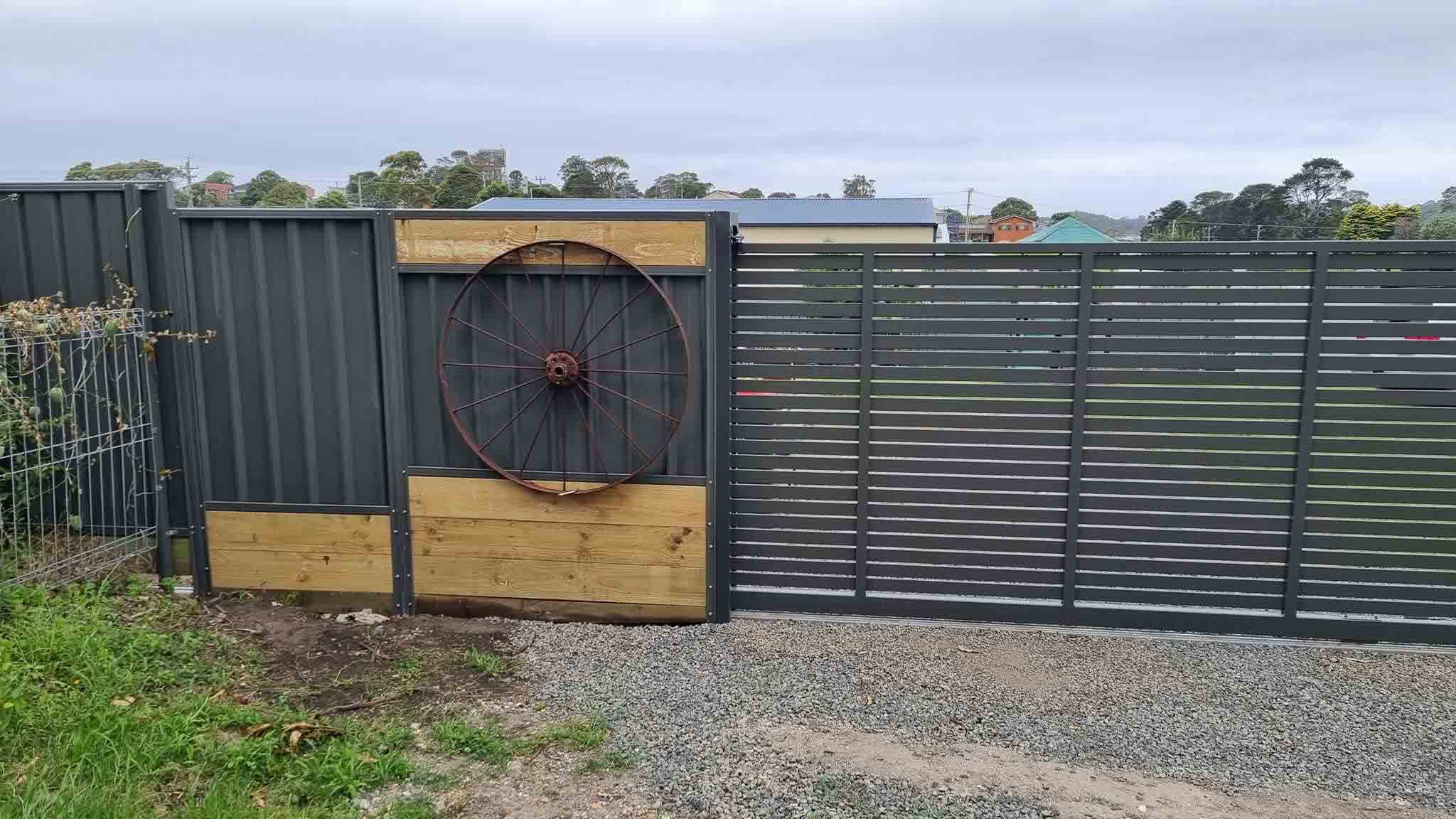 Wide view of a charcoal slat fence and gate with a wagon wheel feature