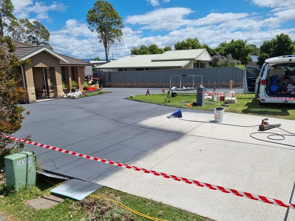 Freshly resurfaced charcoal driveway taped off, with a work van parked alongside