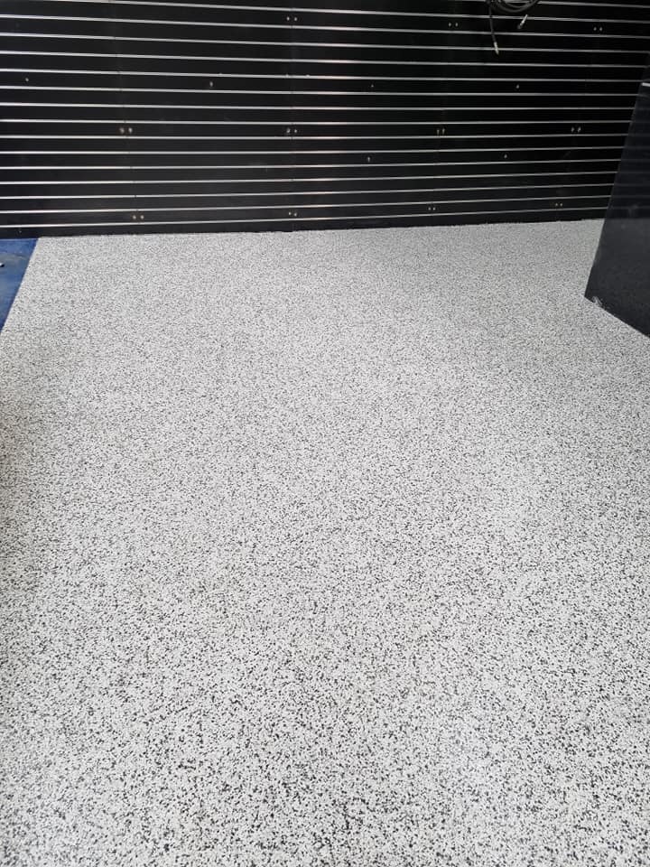 White and grey flake floor coating in front of a dark slatted screen