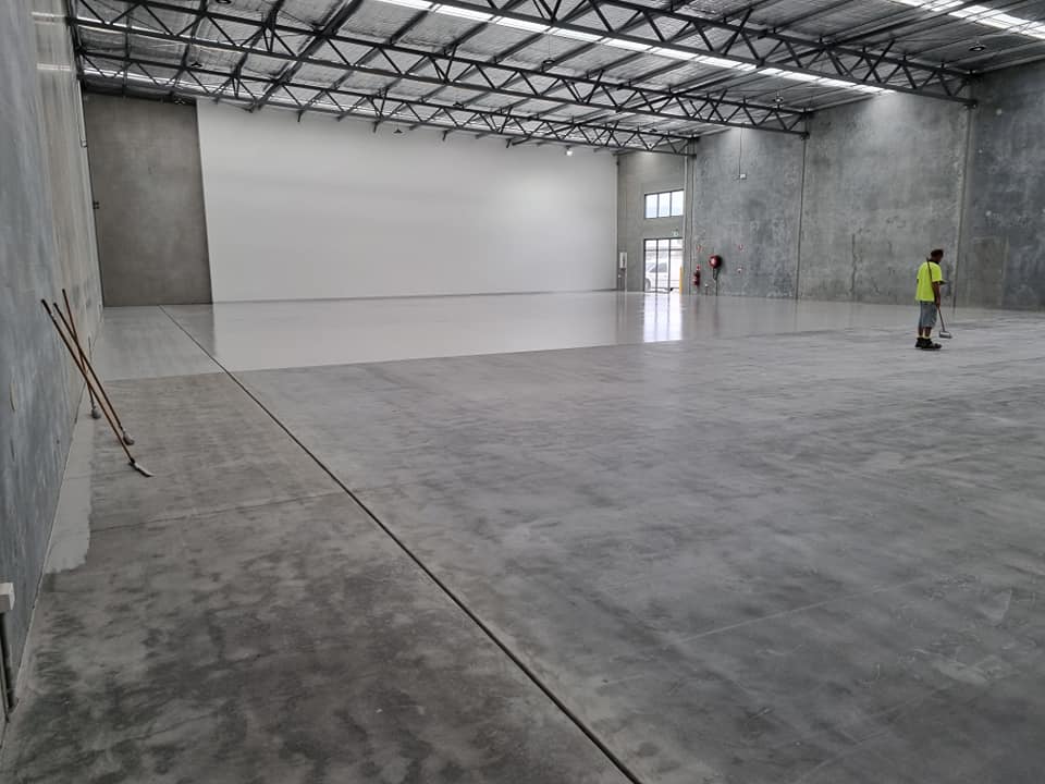 Worker coating a large warehouse floor, ground concrete in front