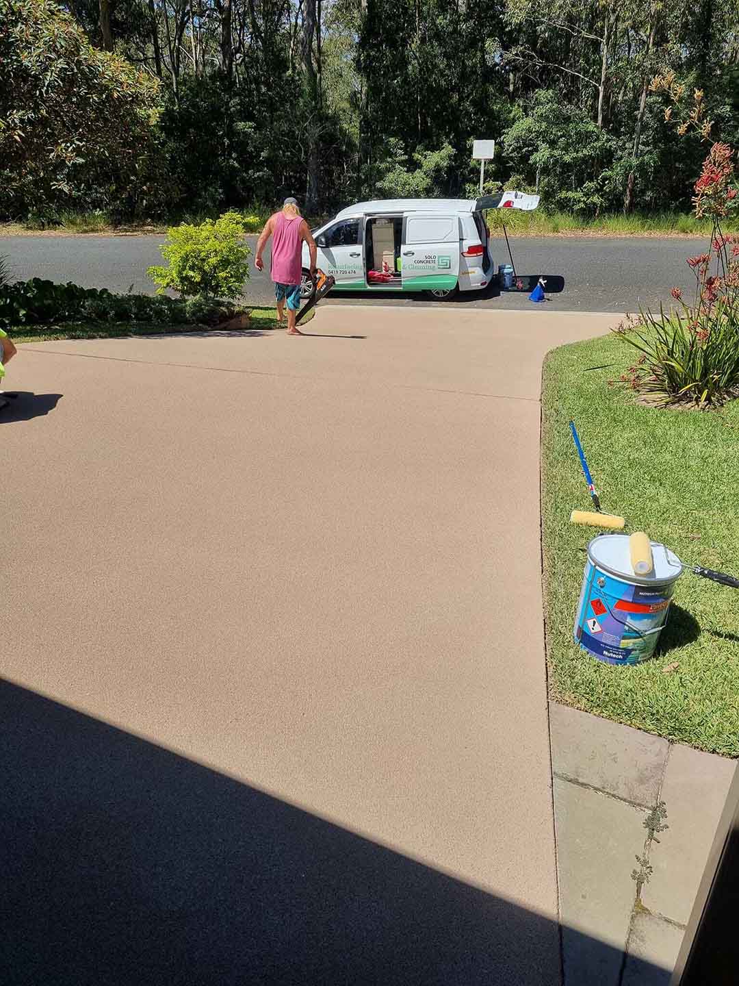 Sandstone-coloured driveway coating with a roller and paint tin on the grass
