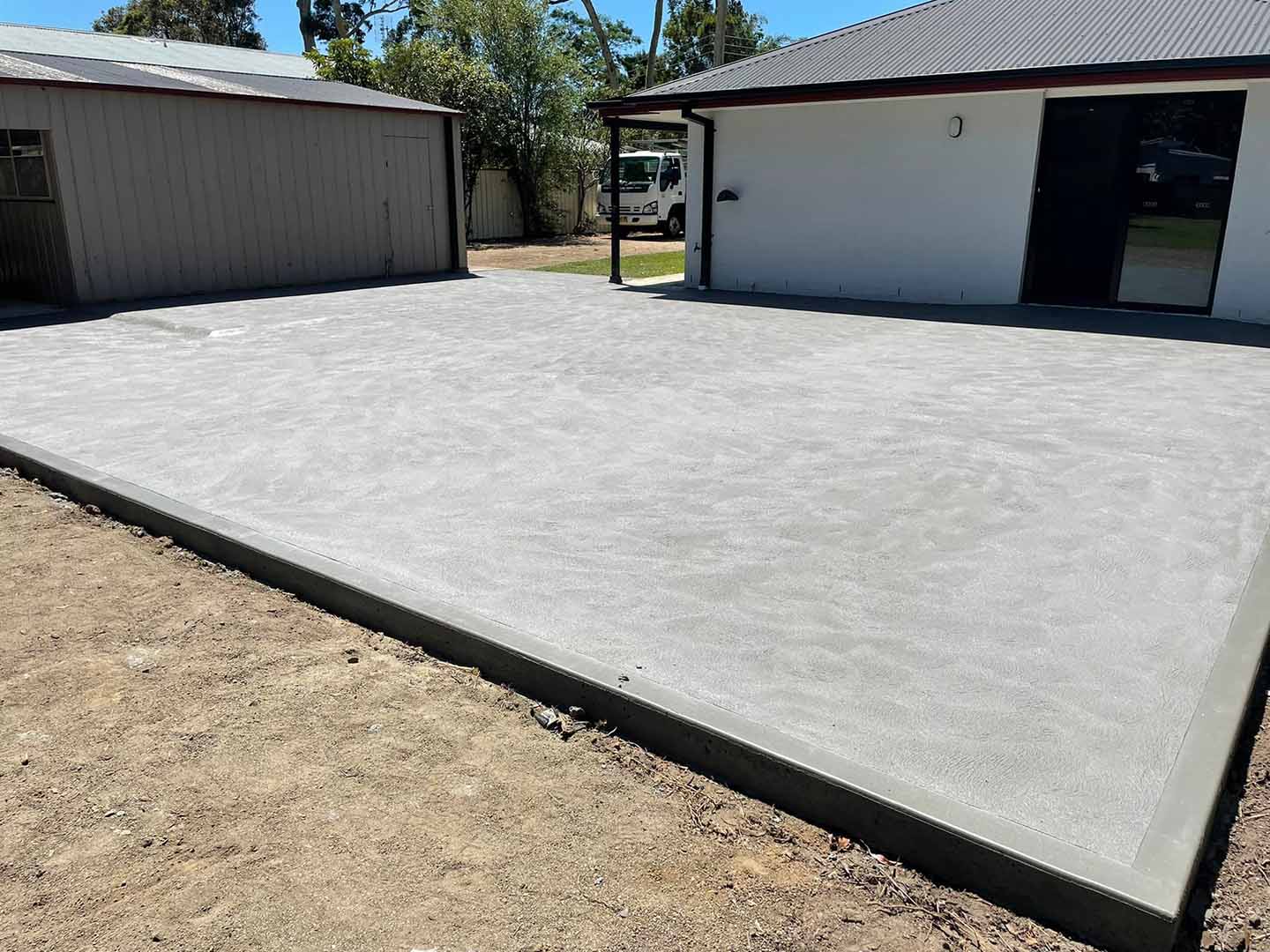 New concrete slab between a shed and a white house