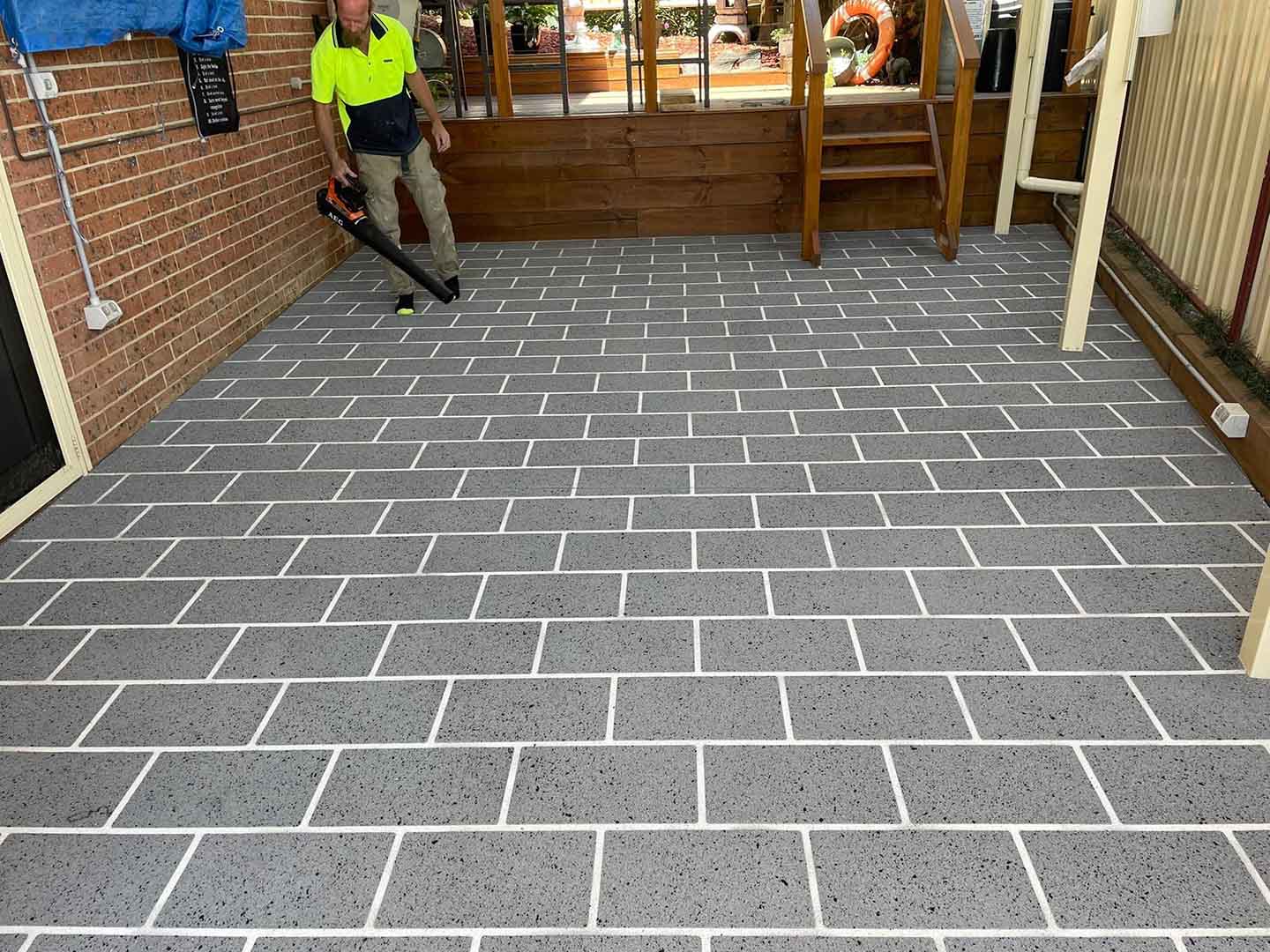 Worker with a leaf blower on a freshly finished tile-pattern patio