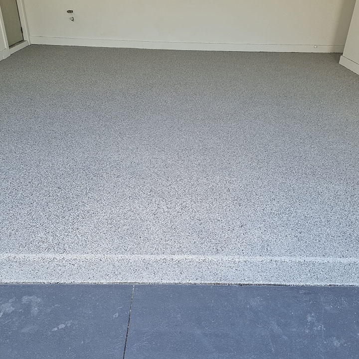 Speckled flake floor coating in a garage, meeting the darker driveway