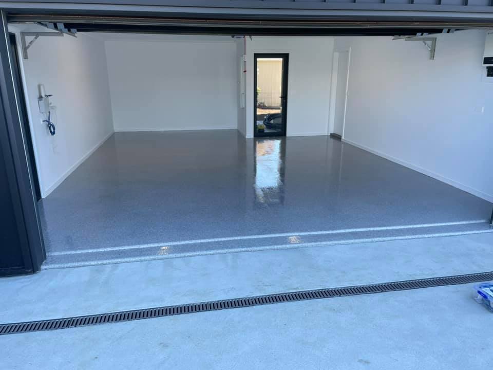Glossy flake floor coating in a garage, seen from the open door with a drain in front