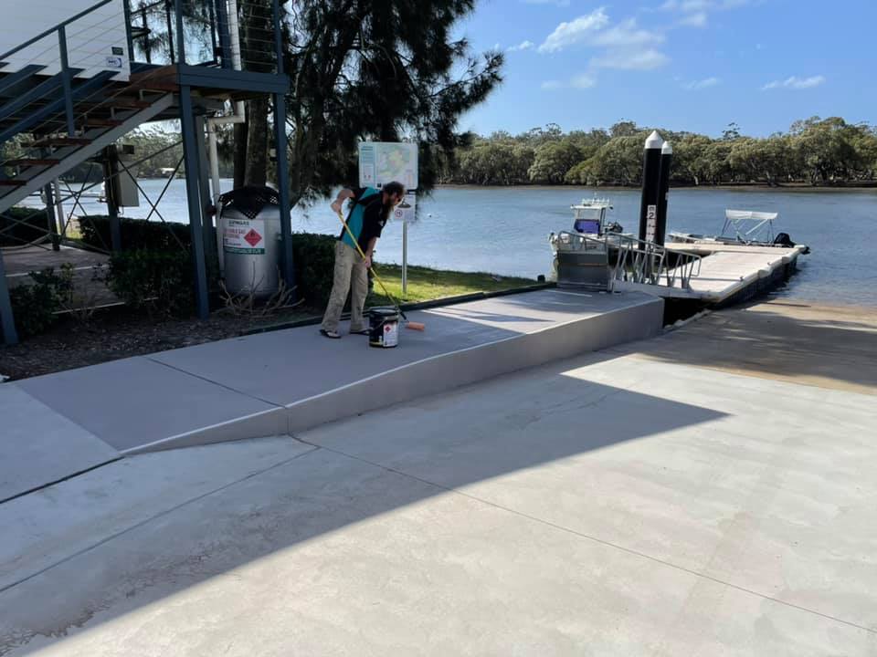 Worker coating a concrete area next to a river jetty