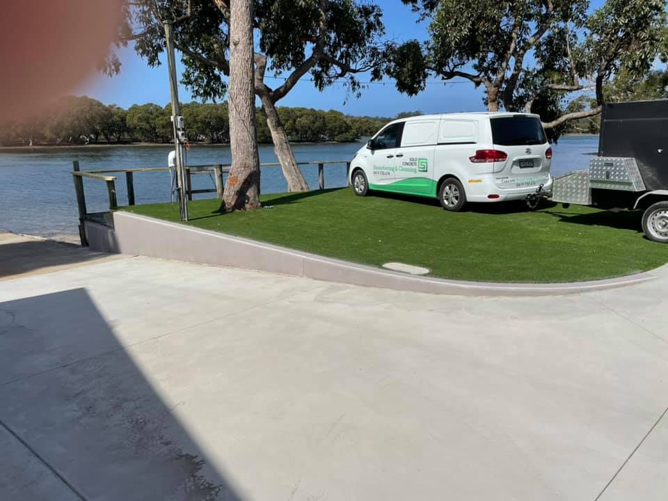 Resurfaced concrete driveway by a river, with a work van on artificial turf