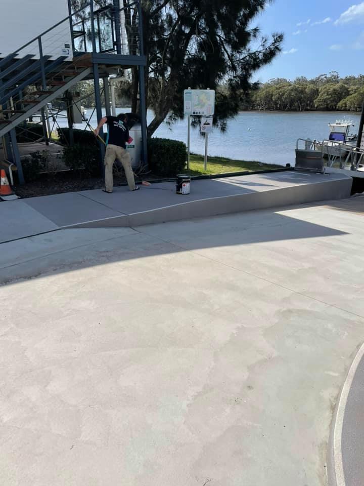 Worker finishing a resurfaced concrete area beside a river