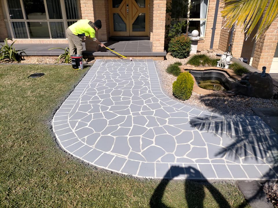 Grey crazy-paving pattern being marked out on a front path beside a pond