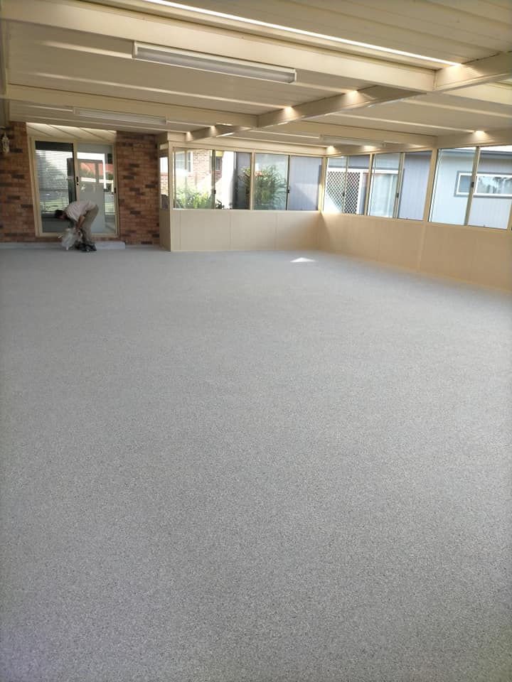 Long sunroom with a new speckled grey floor, worker kneeling at the far end