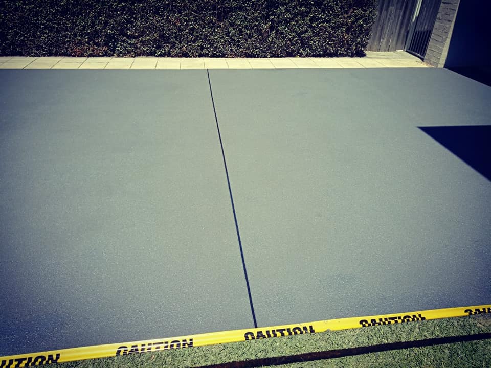 Grey resurfaced concrete area with caution tape along the lawn