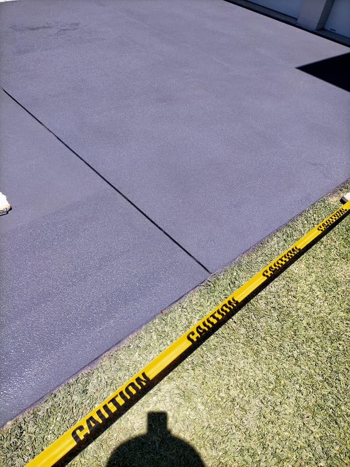 Grey resurfaced concrete with caution tape on the lawn edge, another angle