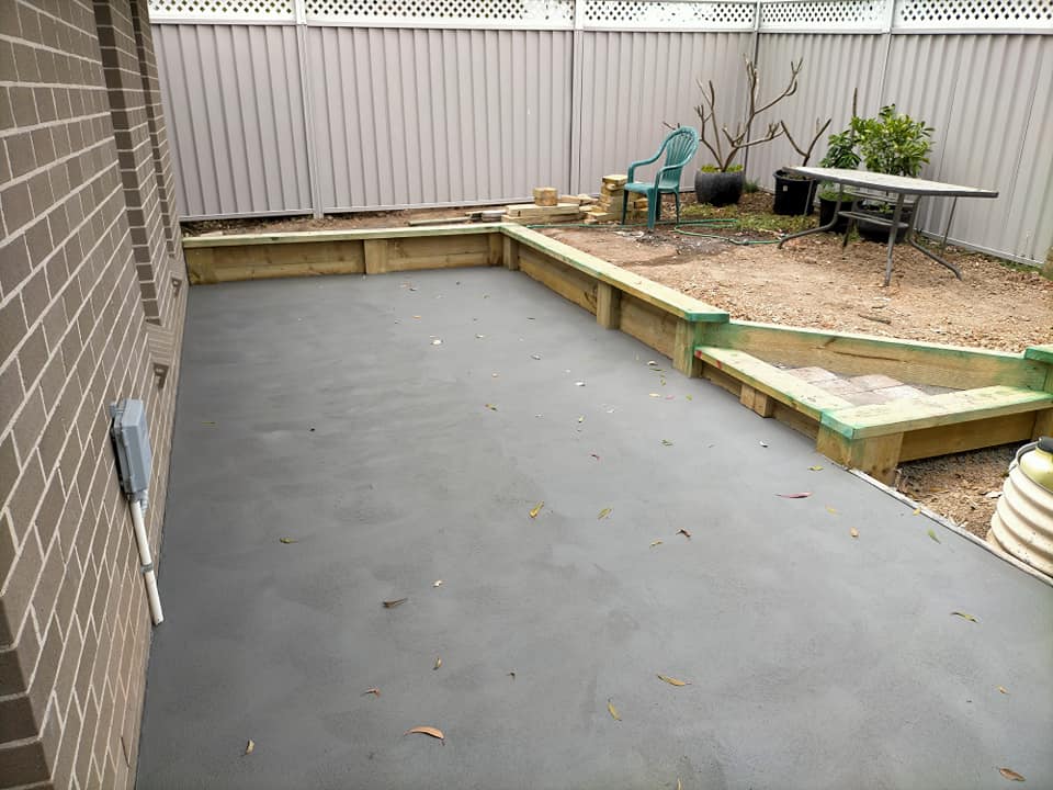 Grey resurfaced courtyard beside a brick wall and timber garden edging