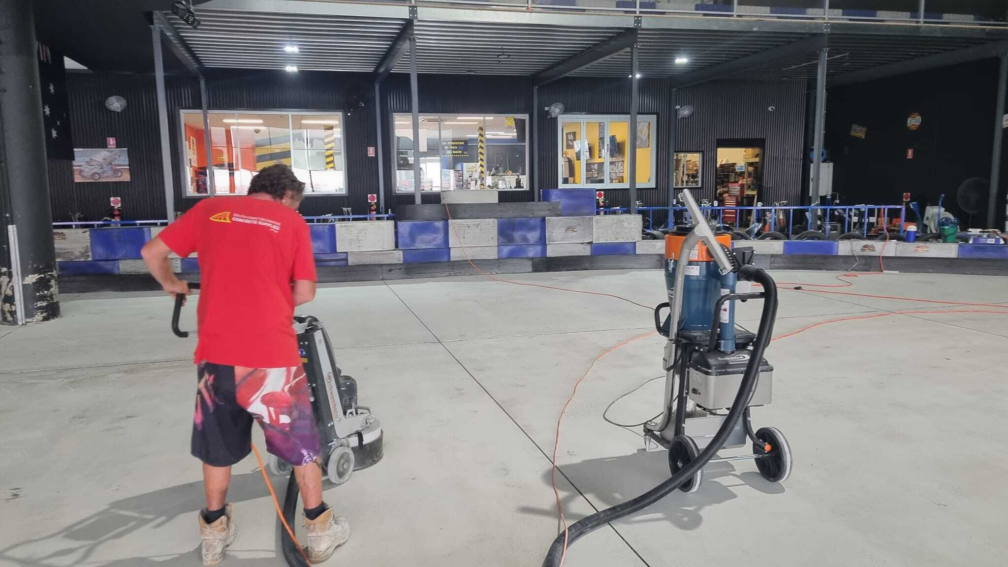 Worker running a floor grinder on the concrete floor of an indoor kart track