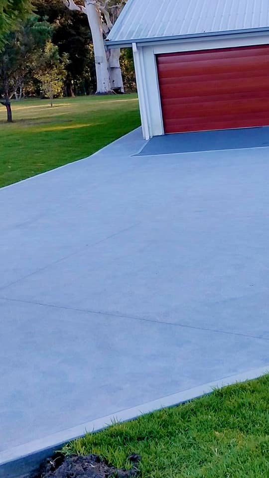 Grey resurfaced driveway leading to a red garage door