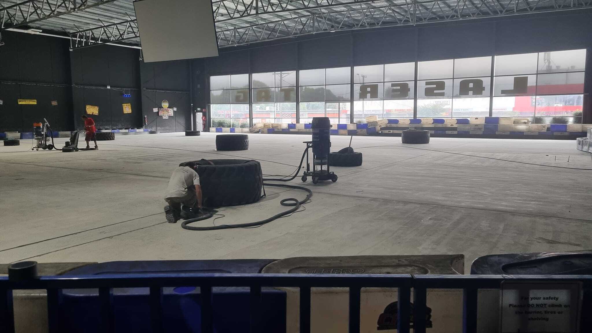 Indoor kart track floor being prepared, with tyres and a vacuum unit on the concrete