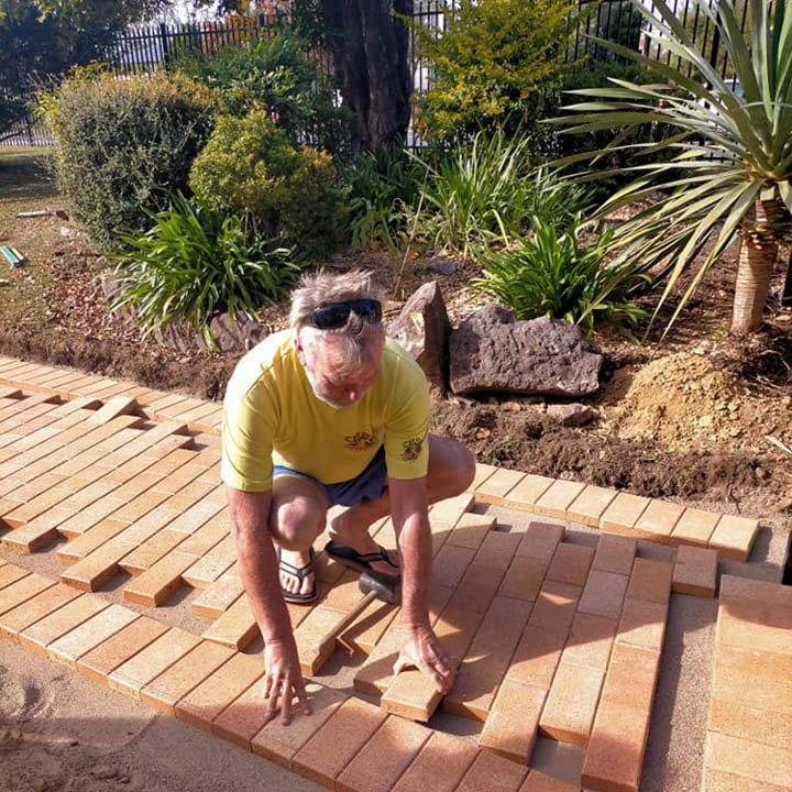 Man kneeling to lay clay pavers along a garden bed