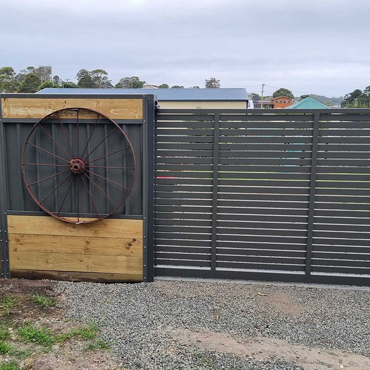 Charcoal slat fence and gate with an old wagon wheel on a timber panel