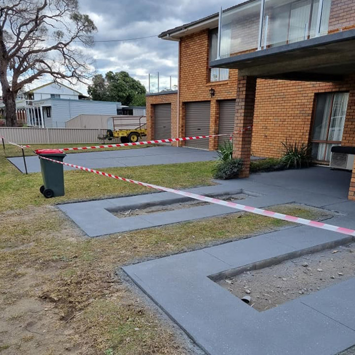 Newly coated charcoal ribbon driveway beside a brick house, taped off