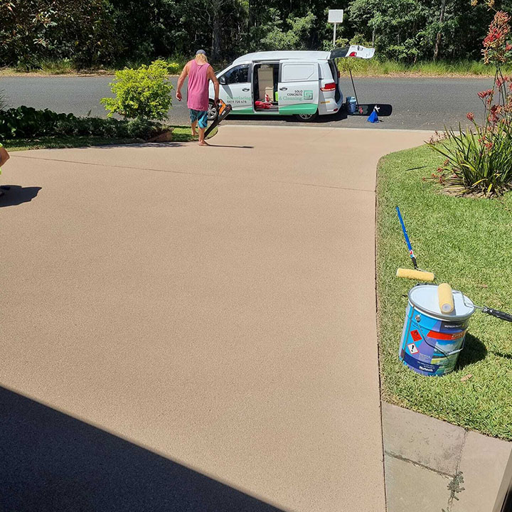 Freshly coated sandstone-coloured driveway with a paint tin and roller on the lawn
