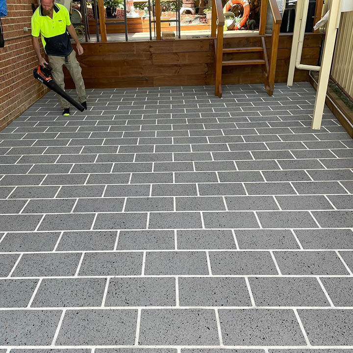 Worker using a leaf blower on a grey tile-pattern resurfaced patio