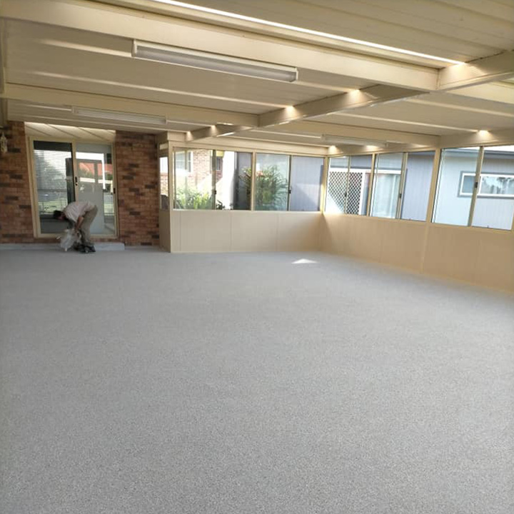 home-about1 Large enclosed room with a new speckled grey floor coating, worker at the back