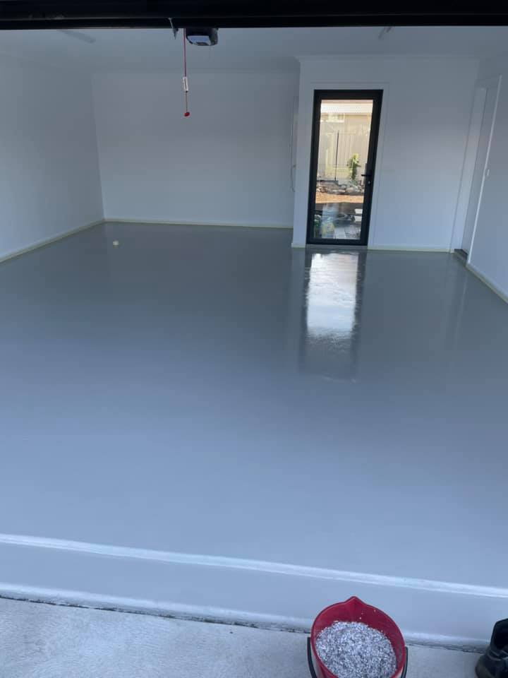 Glossy grey floor coating in an empty garage, bucket in the foreground