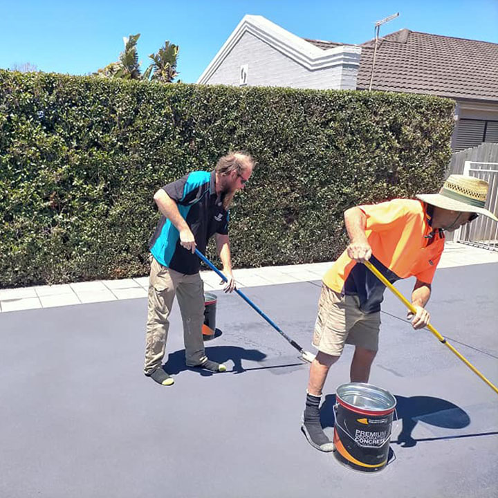 Two workers rolling a grey coating onto a concrete area