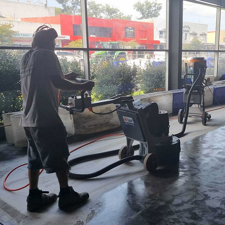 Worker using a floor grinder inside a shop with large windows